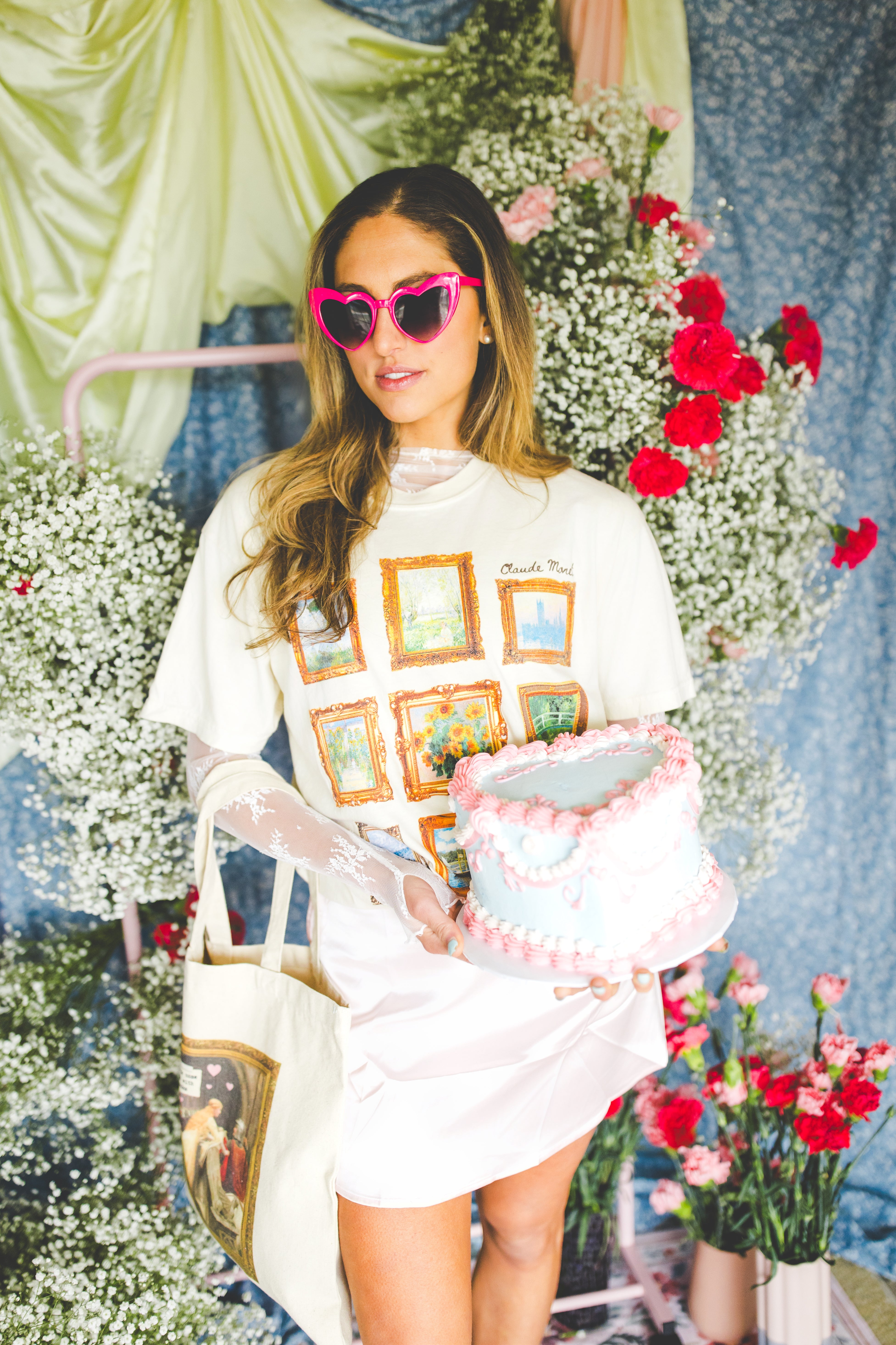 Woman wearing a Claude Monet tee shirt holding a cake with flowers and a decorative background