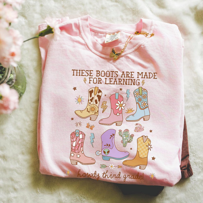 Pink shirt with colorful boot illustrations and text on a soft surface with flowers.