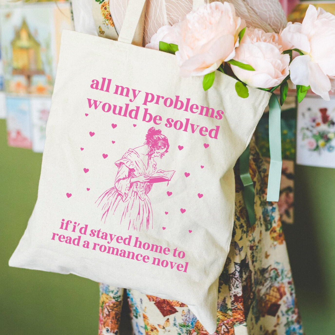 Tote bag with humorous text and graphics, held by a person with flowers, against a green wall.
